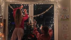 two people standing in front of a window with christmas lights on the windowsills