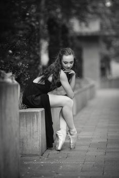 black and white photograph of a young woman sitting on a wall with her legs crossed