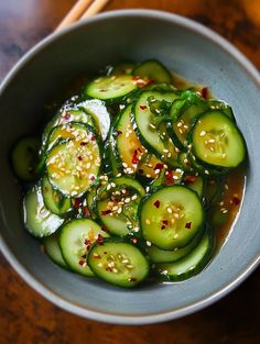 a bowl filled with sliced cucumbers and sesame seeds on top of a wooden table