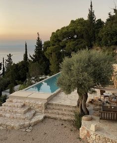 an outdoor dining area next to a swimming pool with olive trees in the foreground