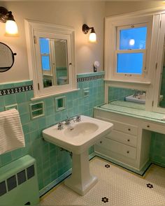 a bathroom with green and white tiles on the walls, sink, mirror and cabinets