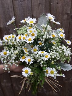 a person holding a bouquet of daisies in front of a wooden fence with grass