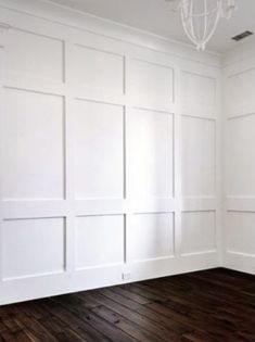 an empty room with wood floors and white walls, including a chandelier hanging from the ceiling