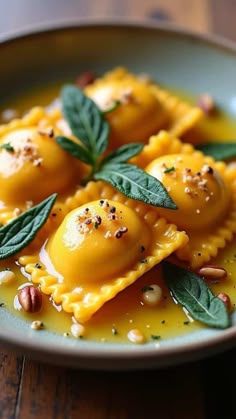 some ravioli with sage leaves and nuts on a blue plate sitting on a wooden table