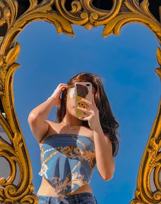 a woman taking a selfie in front of a golden mirror with her cell phone