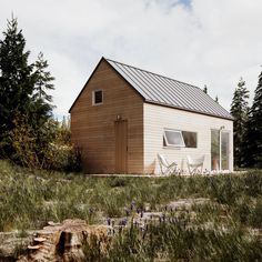 a small wooden house sitting on top of a grass covered field next to trees and bushes