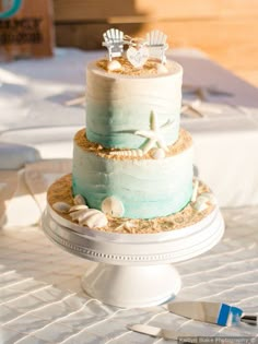 a three tiered cake is decorated with shells and starfish on a tablecloth