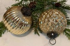 two shiny glass ornaments are hanging from a christmas tree with pine cones on the branches