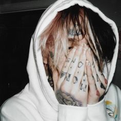 a person with tattoos covering their face and hands in front of them, covered by a white hoodie