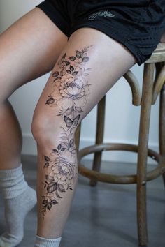 a woman sitting on a stool with her legs crossed and flowers tattooed on the leg