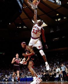 a basketball player dunks the ball in front of his opponent during a game at an indoor arena