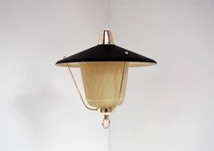 a black and gold light hanging from a ceiling fixture with a white wall in the background