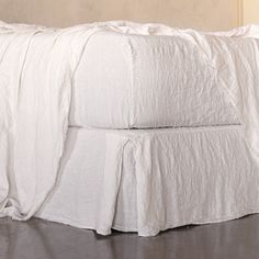 the bed is made with white linens and has a ruffled skirt on it