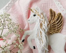 a close up of a white horse on a pink blanket with flowers in the foreground