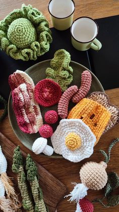 crocheted food items displayed on wooden table next to mugs and utensils