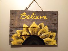 a painted wooden sign with the words believe and a sunflower on it hanging from a rope