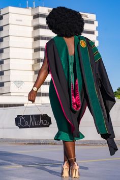 a woman walking down the street in her graduation gown and cap with an afro on it