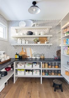 an organized kitchen with white shelves and black counter tops, full of food items on the shelves