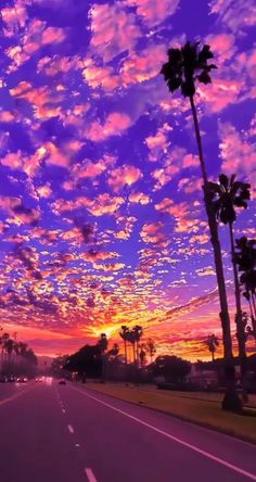 the sun is setting behind palm trees on the side of the road with clouds in the sky