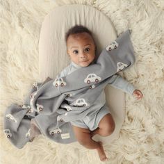 a baby laying on top of a white rug wearing a gray and white car blanket