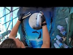 a woman is painting a mural on the side of a wall with dolphins in it