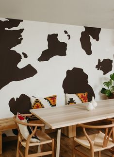 a dining room table with chairs and a cow painted on the wall behind it in black and white