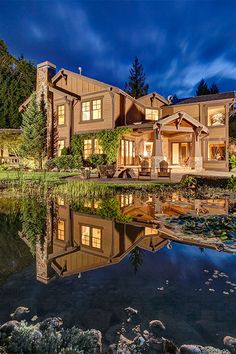 a large house is lit up at night with its reflection in the water's surface