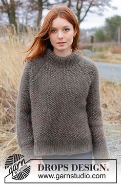 a woman standing in the grass wearing a sweater