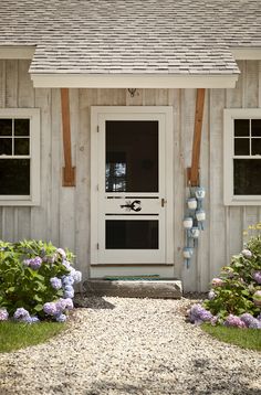 a white house with flowers in front of it and two windows on the side of the house