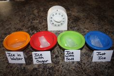 four different colored bowls sitting on top of a counter next to a timer and magnets