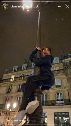 a man sitting on top of a lamp post in front of a tall building at night