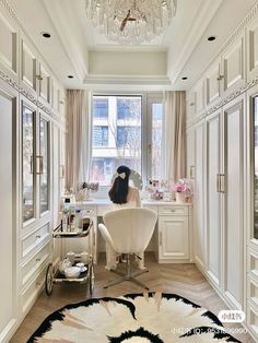 a woman sitting at a desk in front of a window with a chandelier