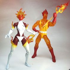 two action figures standing next to each other on a white surface with one holding a fireball