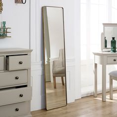 a large mirror sitting on top of a wooden floor next to a white dresser and chair