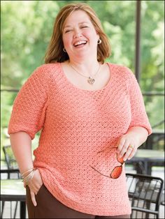 a woman smiling and holding an object in her hand while standing next to a table