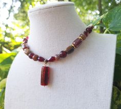 A beautiful gemstone and glass beaded pendant choker necklace, consisting of earthy shades of brown, red, and gold. Gemstones: Brown banded agate stone pebbles, tiger's eye stone pebbles, gold hematite. Glass: Fire-polished red cylinder Czech glass beading, dark red rondelle Czech glass beading, brown faceted cylinder glass beading, diamond pressed red Czech glass beading, red and brown Czech glass, red and gold cylinder Czech glass pendant. *Handmade by me, one of a kind. *Hypoallergenic 24k gold plated stainless steel chain and clasp.  Nickel Free. *Total Length: 14.5 inches *Length of Chain: about 13 inches *Extender Length: 1 inch. Please let me know if you require a longer extension chain to ensure a proper fit!  Just let me know how long you would like your necklace under personaliza Amber Beaded Necklaces With Spacer Beads As Gift, Amber Czech Glass Beaded Necklace Gift, Cottagecore Fairy, Fairy Necklace, Pendant Choker, Witchy Jewelry, Eye Glass, Banded Agate, Tiger Eye Stone