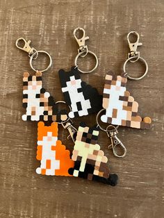 four pixel key chains are sitting on a wooden surface, one is orange and the other is black