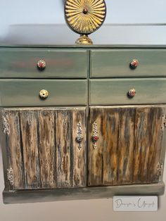 an old dresser has been painted green and gold with knobs on the doors, along with a sunburst decoration