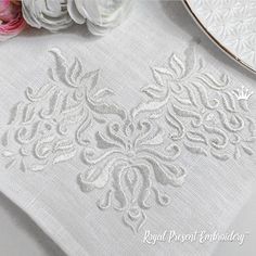 the table cloth has been embroidered with white thread and is next to some pink flowers