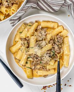 two bowls filled with pasta and meat on top of a white plate next to silverware