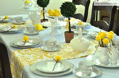 the table is set with yellow flowers and white dishes