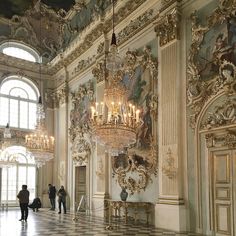 people are standing in an ornate room with chandeliers and paintings on the walls