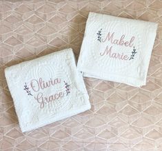 two white towels with embroidered names on them sitting on top of a quilted surface