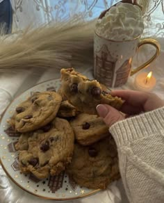 chocolate chip cookies on a plate next to a coffee cup and teacup with a lit candle