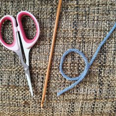 two pairs of pink scissors sitting on top of a piece of cloth next to knitting needles