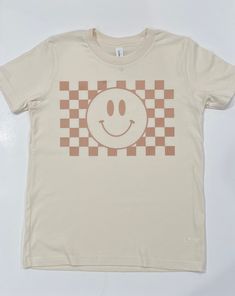 "Bringing back that 90's vibe with our new checkerboard smiley face! This tee is a Bella + Canvas brand youth shirt in the color Natural, with \"tan\" graphic.  WASH & CARE INSTRUCTIONS:  To maintain the integrity of the shirt, we suggest washing inside out in cold water with like colors, using a mild/color safe detergent. Dry on low heat or the \"delicate cycle.\" Please do not bleach or dry clean. If ironing, use on low setting and do not iron directly onto the decal/lettering. A wash and care Smiley Faces, Kids Graphic Tees, Inspiration For Kids, Happy Face, Having A Baby, Smiley Face, Smiley, Kids Shirts, Bella Canvas