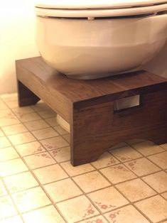 a white toilet sitting on top of a wooden stand in a bathroom next to a tiled floor