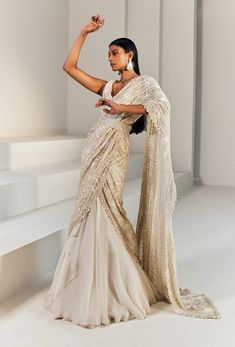 Editor's Note Ivory And Gold Pre-stitched Lehenga Saree Paired With A Fitted Blouse And Belt. Color: Ivory Gold Fabric: Net, Cupro, Organza, Crepe, Double Georgette . Embroidery Details: Bead, Thread, Resham & Bugel. Care: Dry Clean Only About the Designer Ritika Mirchandani is known for its clothes that are wearable and luxurious with a feminine and glamorous feel to them. Luxury Bollywood Saree With Cutdana, Luxury Designer Lehenga Saree, Luxury Silk Lehenga With Sheer Dupatta, Luxury White Pre-draped Saree With Dori Work, Luxury Silver Pre-draped Saree With Sheer Dupatta, Luxury Pre-draped Saree With Sheer Dupatta For Festivals, Luxury Designer Pre-draped Saree With Dupatta, Luxury Saree With Cape Sleeves For Reception, Luxury Unstitched Saree For Reception