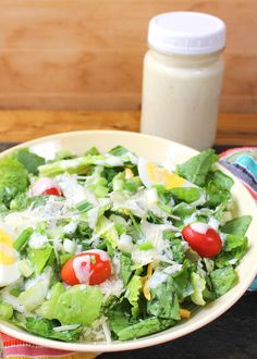 a salad with tomatoes, lettuce and cheese in a bowl next to a bottle of dressing