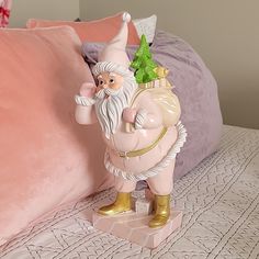 a pink bed topped with pillows and a statue of an old man holding a christmas tree